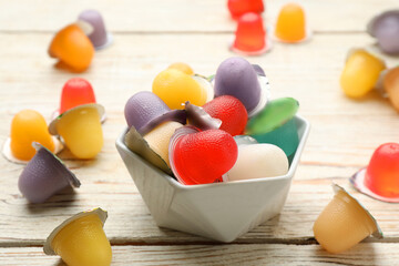 Bowl with tasty bright jelly cups on white wooden table