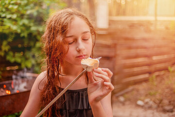 Food in nature. A teenage girl eats marshmallow roasted on a fire in the forest.