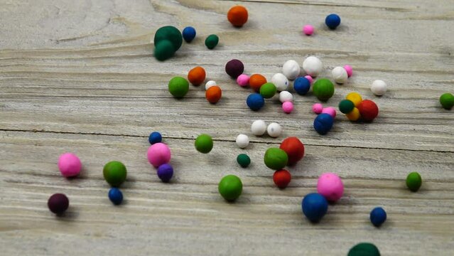 Multi colored plasticine balls fall and roll on the gray wooden board, slow motion. 