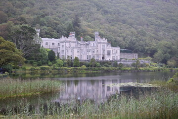 Fototapeta na wymiar Kylemore Abbey on the lake. Small water reflection. Trees and forest on the background. White historical building. Calm pond.