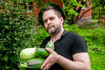 Portrait of a man harvesting organic vegetables.The gardener holds ripe, juicy zucchini in his hands	
