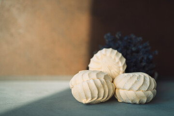 Three handmade marshmallows on a gray table and a bouquet of lavender in the background and a bright sun.