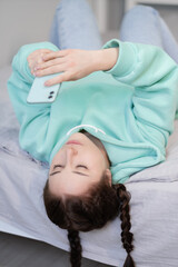 Obraz na płótnie Canvas remote working or distant studying from home. young brunette woman girl blogger on bed with turquoise modern phone . quarantine restrictions. covid-19 pandemic.