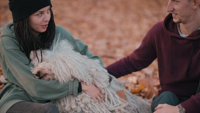 Couple playing with dog. Young happy couple petting their pet while sitting on fallen leaves. Hungarian Shepherd Dog Buli breed in nature.