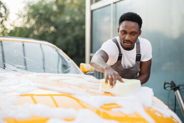 Young attractive African American man washing his modern luxury car in a self-service car wash...