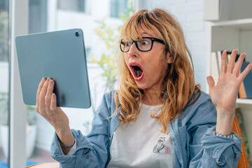 astonished or surprised woman looking at computer or tablet at home