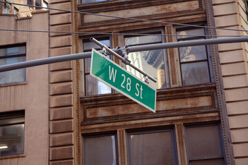 Green big West 28th Street sign hanging on a arch pole in the streets of midtown Manhattan