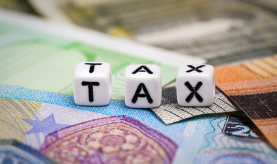 Small white beads with black letters TAX on euro banknotes, closeup detail