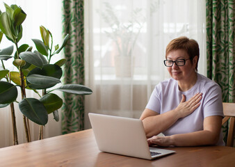 An adult woman sits at a laptop and communicates via video link in sign language. Presses hand to...