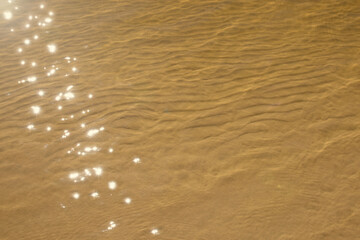 Yellow sand in the shallow waters of the sea. Small dunes on the sand under clear light water. The sun glare is reflected on the water.