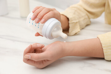 Woman checking infant formula temperature at white table, closeup. Baby milk
