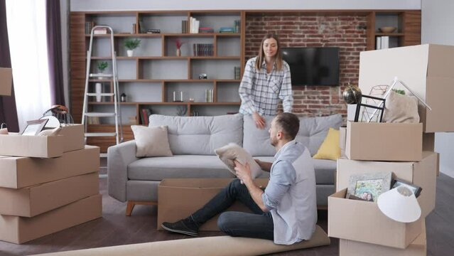 Young couple unpacking cardboard box and discussing interior design in new apartment on moving day. Happy homeowners on relocation day. Real estate and tenancy concept. Loan mortgage for young family.
