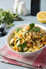 Salad with smoked fish, corn, onions and mustard in a white bowl on light blue background