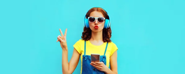 Foto op Canvas Portrait of young woman in headphones listening to music with phone on blue background © rohappy