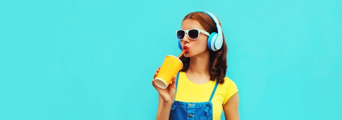 Poster Portrait of young woman in headphones listening to music with phone on blue background © rohappy
