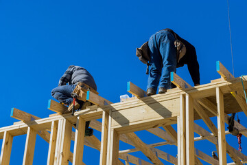 Worker in holding plank installing it on household construction using air hammer in nailing wooden...