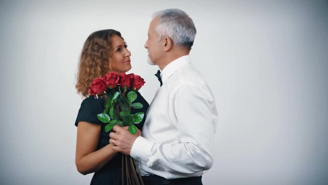 A happy dancing middle-aged couple in love with a bouquet of scarlet roses in their hands on a white background. Celebrating Valentine's Day, anniversary, birthday