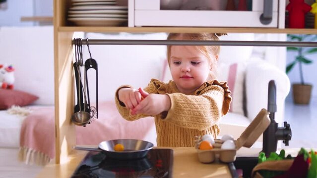 cute little baby girl playing on toy kitchen, pretending to fry the eggs in the morning