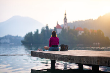 Lone girl sitting on a wooden jetty. Tranquil scene with meditating woman with the beautiful landscape in the background.