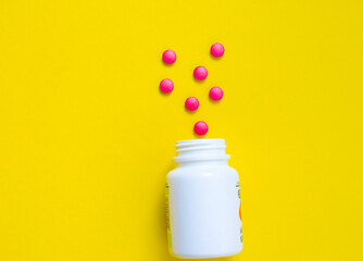 red pills from a jar on a yellow background