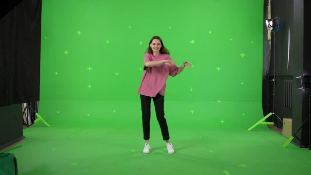 Young woman dancing on a green screen background. Girl makes a gesture with her hands as if swipping the page to the side . Chroma key