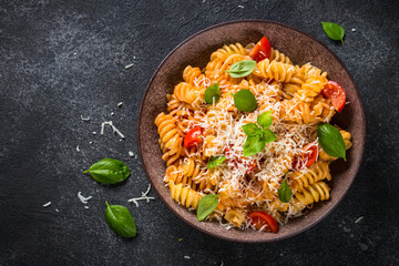 Italian pasta alla arrabiata with basil and parmesan cheese on dark table. Fusilli pasta with tomato sauce arrabbiata. Top view.