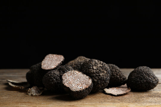 Whole and cut truffles on wooden table against black background