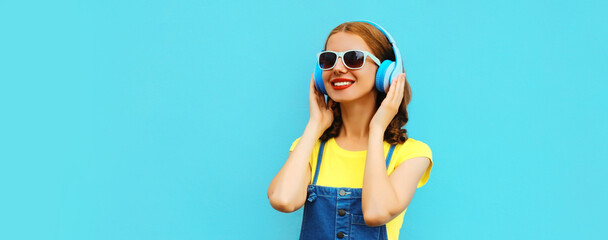 Portrait of happy smiling woman listening to music in headphones on colorful blue background