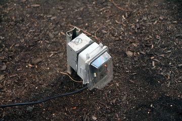 Outdoors public electric outlet with rain cover and a black plugged cable