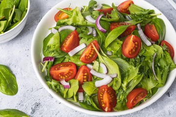 Summer green salad in white bowl plate on grey table
