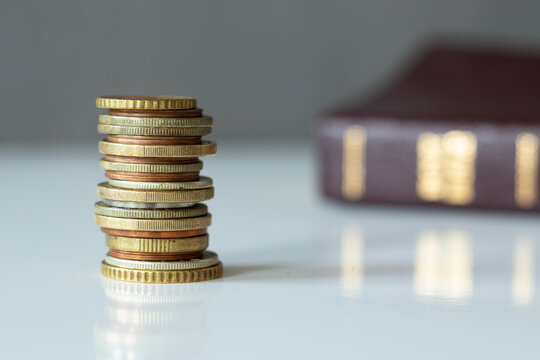 A Stack Of Coin Money With Holy Bible Book In The Background. The Biblical Concept Of Christian Offerings, Tithing, And Gifts In The Church Of God Jesus Christ. A Close-up.