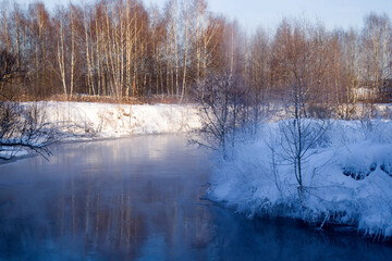 Winter landscape in the Moscow region. The Pekhorka River with non-freezing water. Snow-covered shores, steam rising from the water. 
