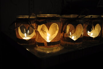 Romantic night still life with handmade candles inside glass jars with paper cut out hearts. Love concept Valentine Day