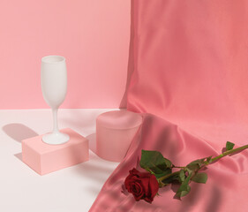 Romantic pastel pink Valentine's Day composition with wine glass, satin curtain and red rose flower. Suitable for Product Display and Business Concept. Modern aesthetic.