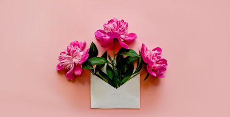 White envelope with pink peonies inside on a pink background.