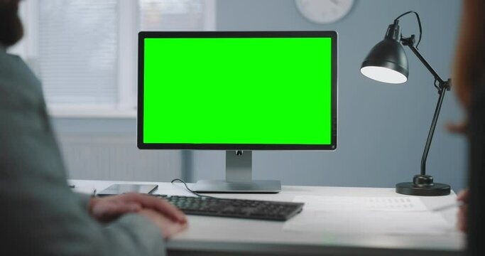Over shoulder view of two business partners using pc with chroma key monitor during meeting at office. Focus on black green screen of computer.