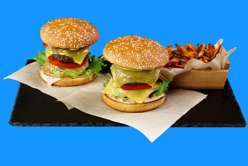 two Big burgers and sweet potato isolated on black stone plate. blue background. close up