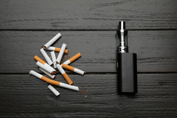 Broken cigarettes and vaping device on black wooden background, flat lay. Smoking alternative © New Africa