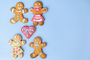 Heterosexual cookie couples, boys and girls and gingerbread heart with icing on the blue background with copy space. Cookies for St Valentines Day