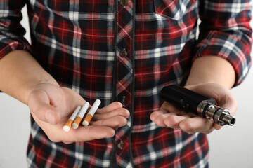 Man with cigarettes and vaping device on light background, closeup. Smoking alternative