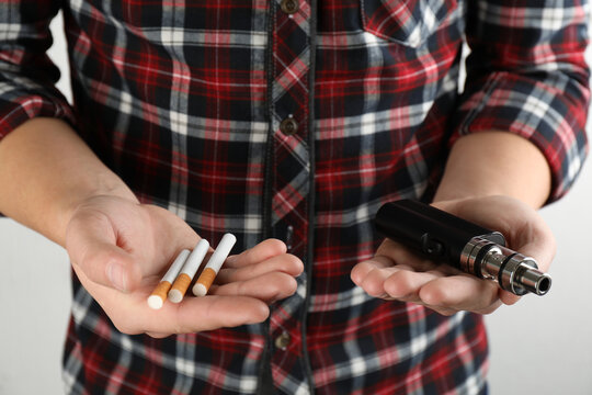 Man with cigarettes and vaping device on light background, closeup. Smoking alternative