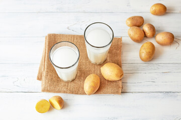 Two glasses of potato milk on a gray background next to fresh potato tubers. Alternative milk....