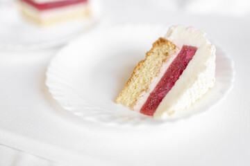 A white-pink piece of cake lies on a white plate on a light background. Delicious pastries