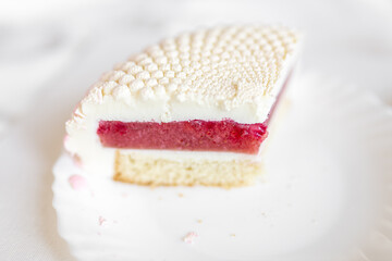 A white-pink piece of cake lies on a white plate on a light background. Delicious pastries