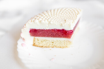 A white-pink piece of cake lies on a white plate on a light background. Delicious pastries