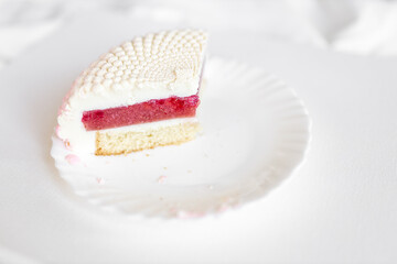 A white-pink piece of cake lies on a white plate on a light background. Delicious pastries