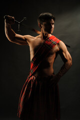 The sexy highlander is posing indoor wearing a medieval costume and holding a sword. 