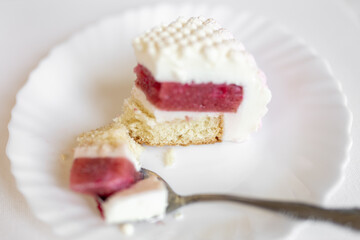 A white-pink piece of cake lies on a white plate on a light background. Delicious pastries