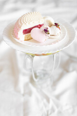 A white-pink piece of cake lies on a white plate on a light background. A pink heart-shaped cake lies on a white plate on a light background. Light macaroons on a white canvas. Delicious pastries