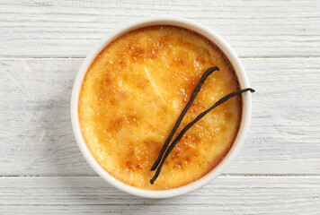 Delicious creme brulee and vanilla sticks on white wooden table, top view